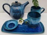 Joffre teapot, two mugs, a small dish and a tray by Matthew Freed, with a white flower and a fern